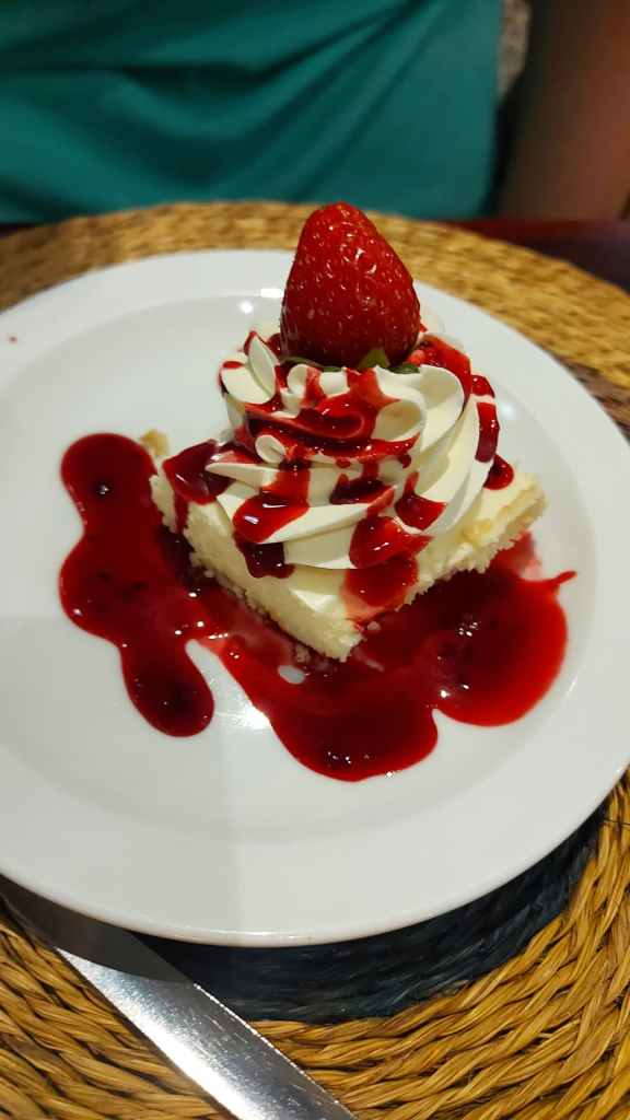 gorgeous cheese cake smothered in a red sauce with a strawberry on top